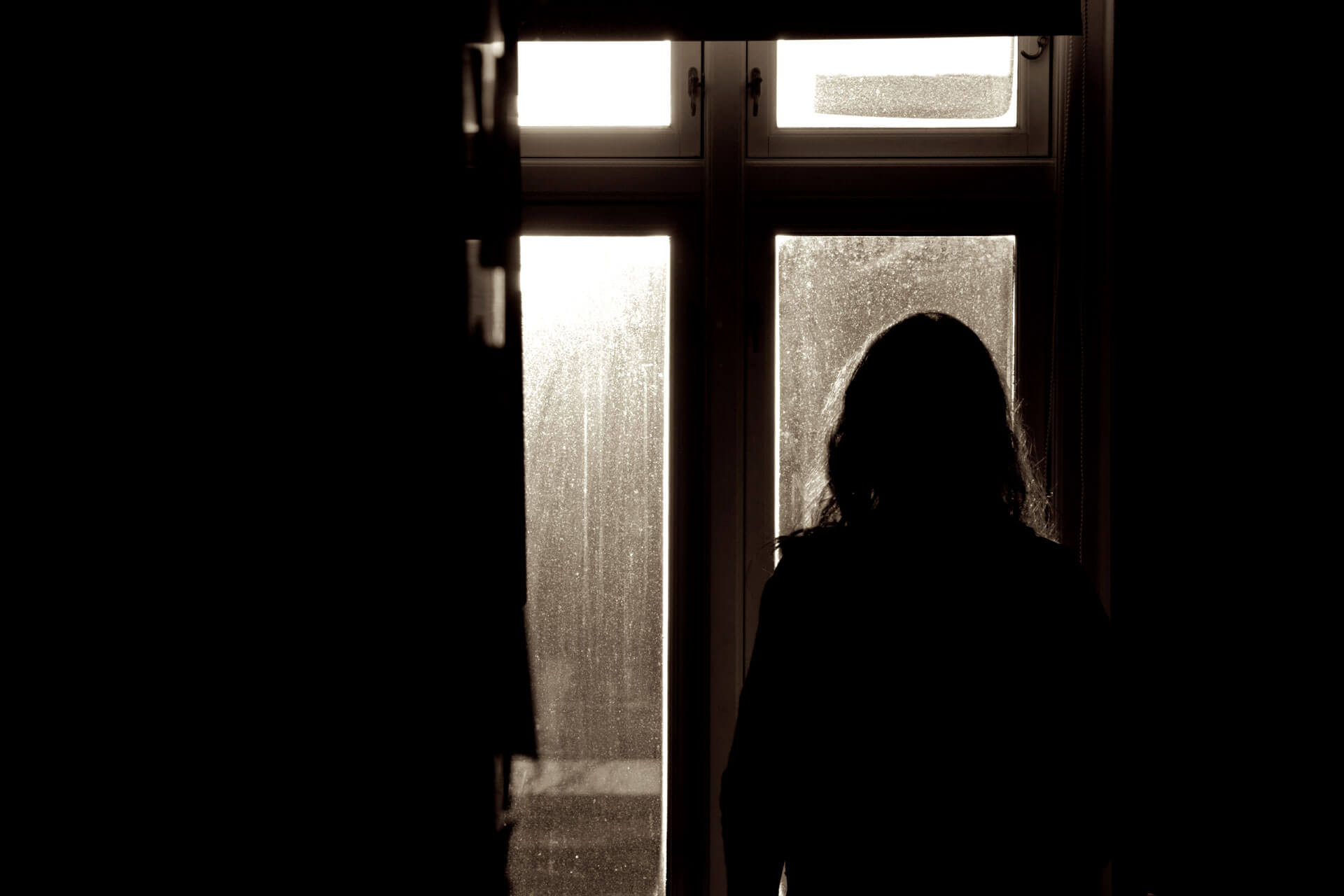 A silhouetted woman stands facing a window