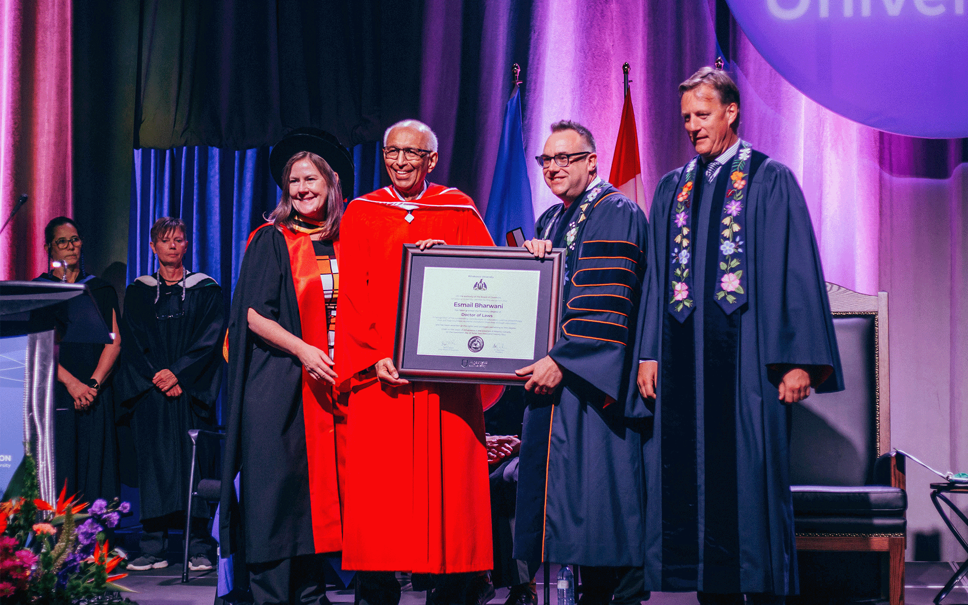 A woman and three men standing together with one of them holding a large framed document for Esmail Bharwani's Honorary Doctor of Laws during the convocation ceremony