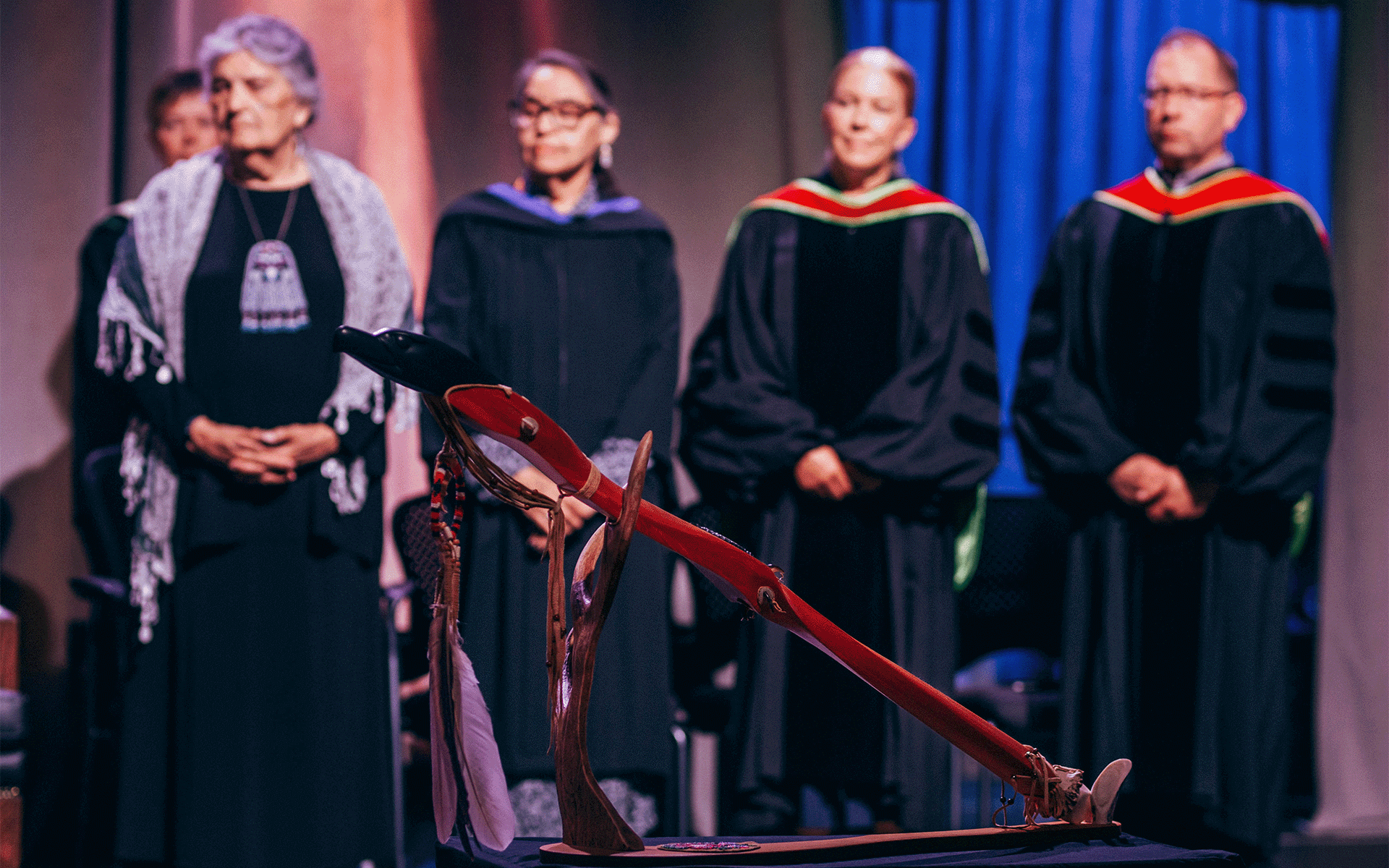 Four people sitting in the background during the convocation ceremony and the image is focused on the Athabasca University Mace