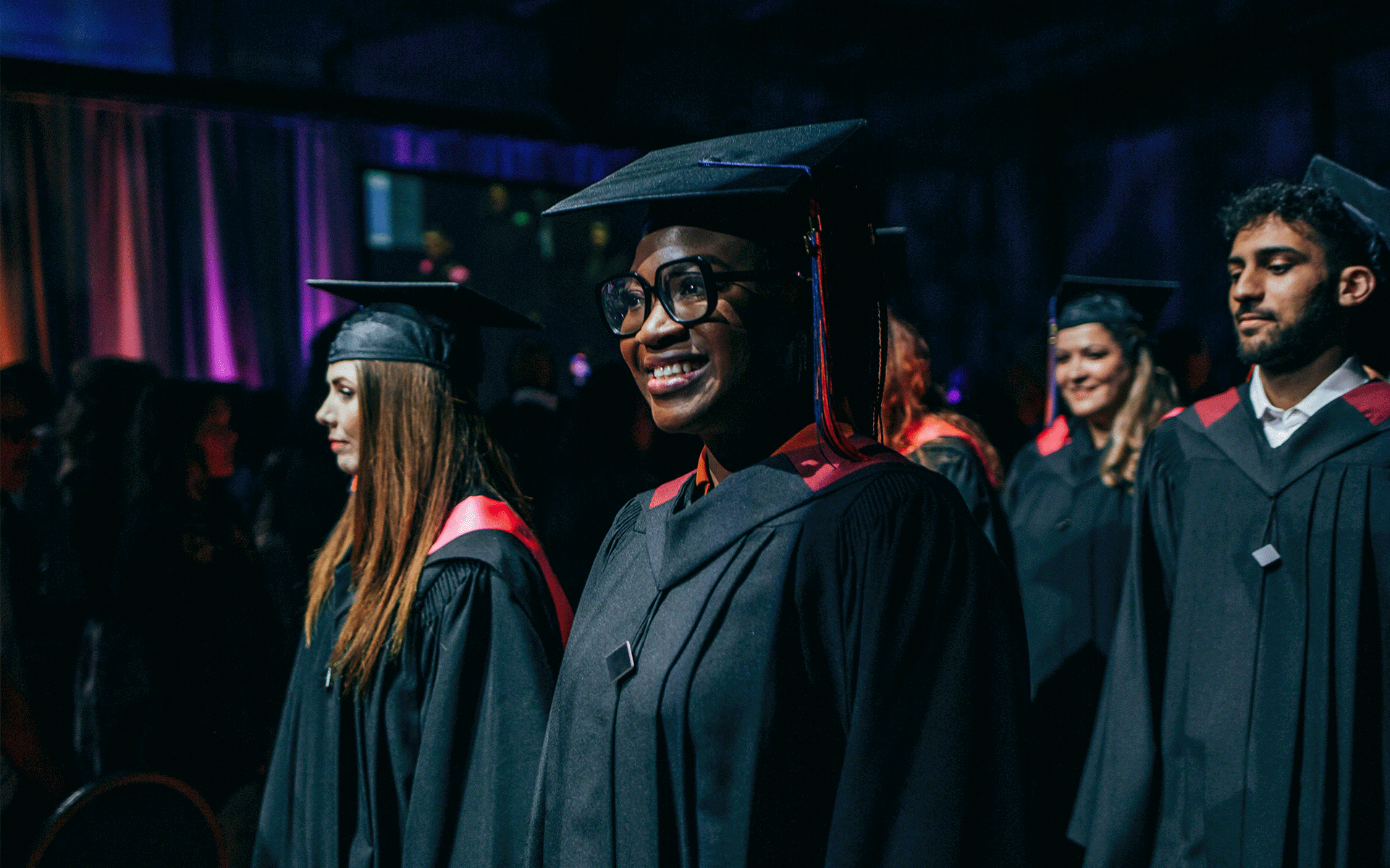 Graduates walking into the ceremony in a procession. Image is focused on a smiling woman