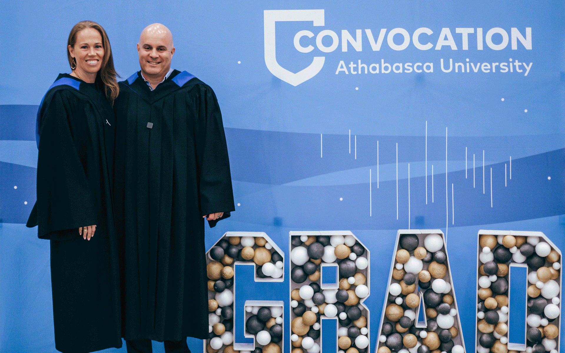 a man and woman who are both graduates standing in front of a convocation sign