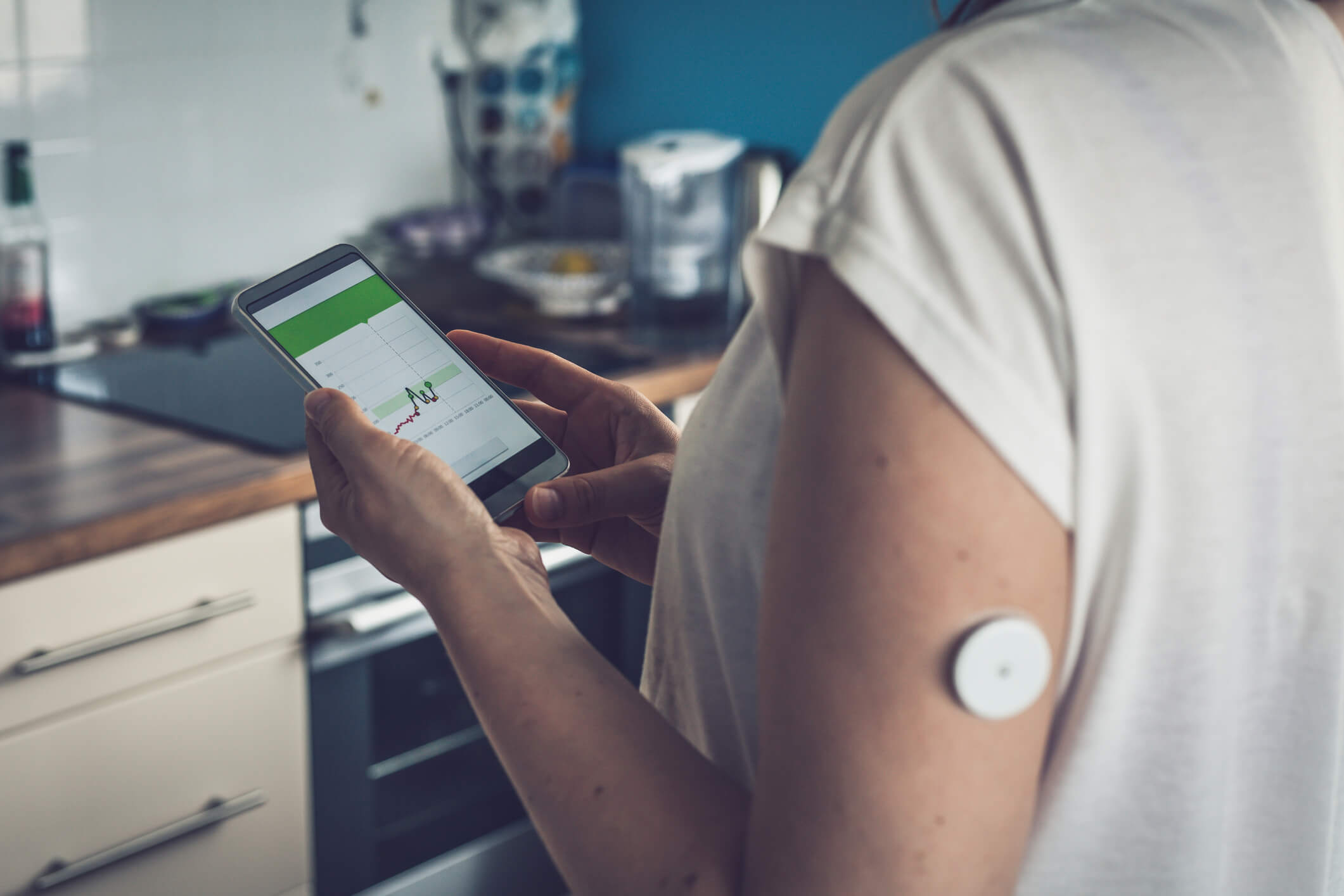 Woman checking glucose level with a remote sensor and mobile phone, sensor checkup glucose levels without blood, good result. Diabetes treatment. Focus on background.