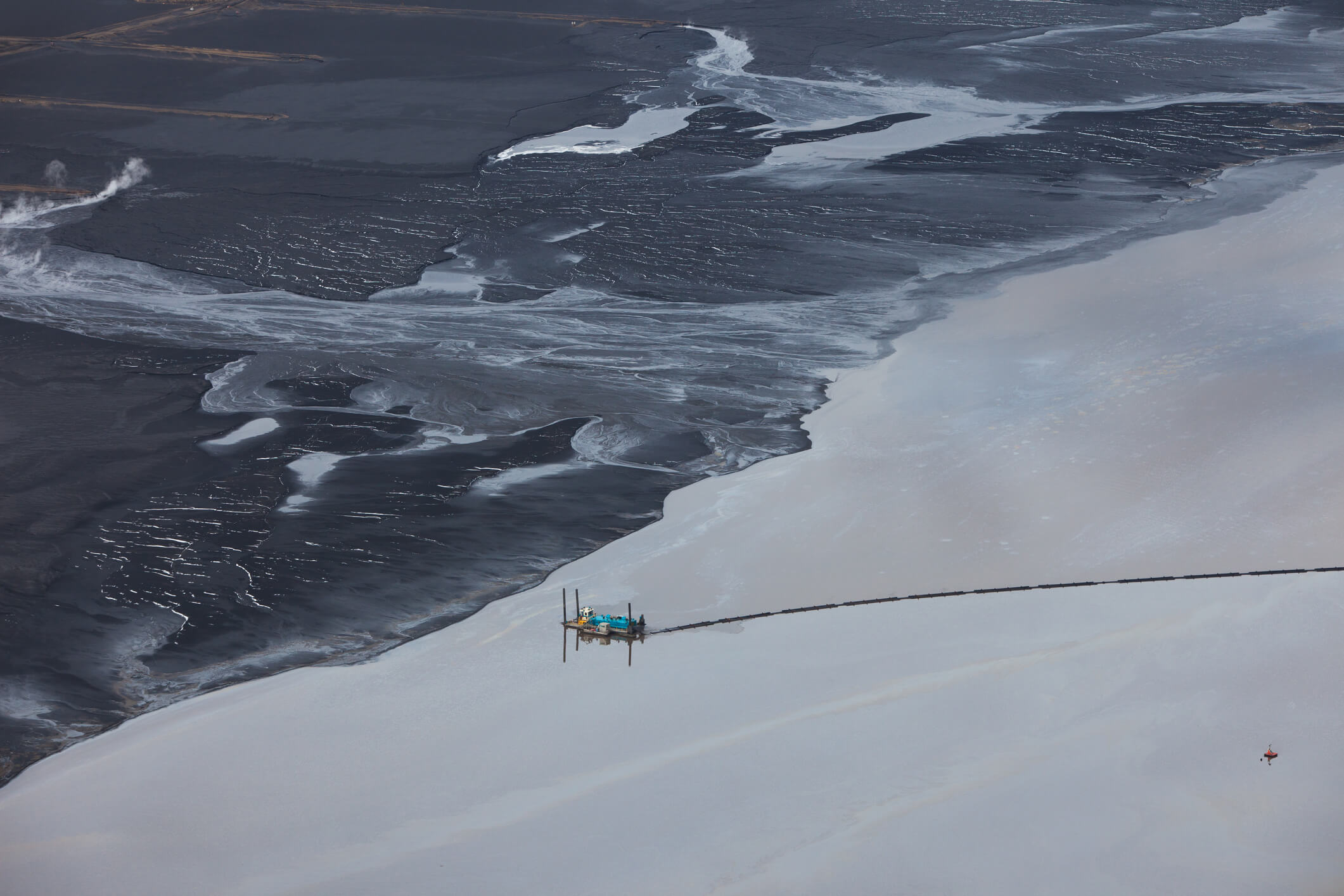 Crude oil seen separated from sand for collection. Tailings ponds are used to separate the heavy oil bitumen from the sticky sand mined from around the area. Near Fort McMurray, Alberta.