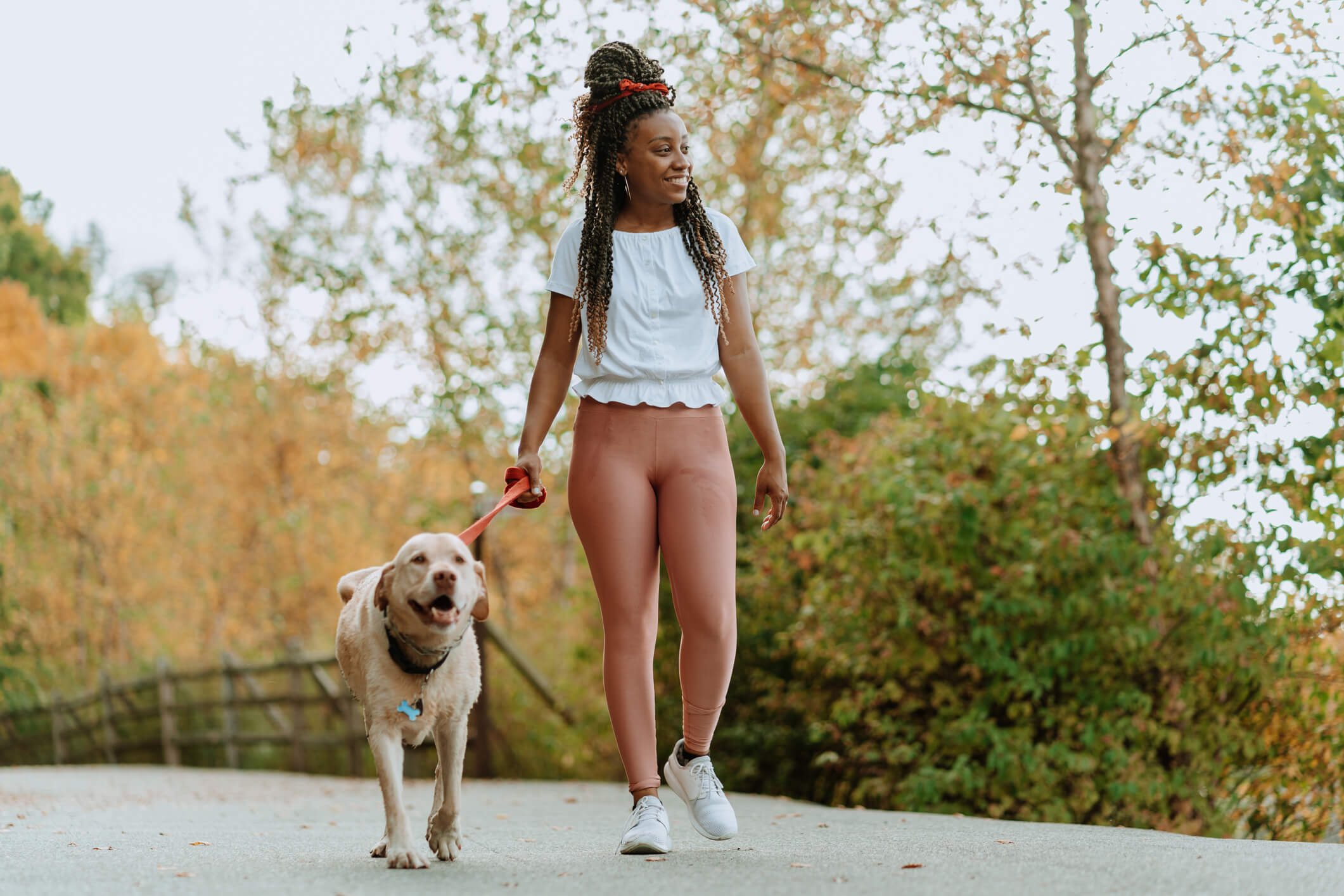 Black woman walking a dog in a tree-lined area