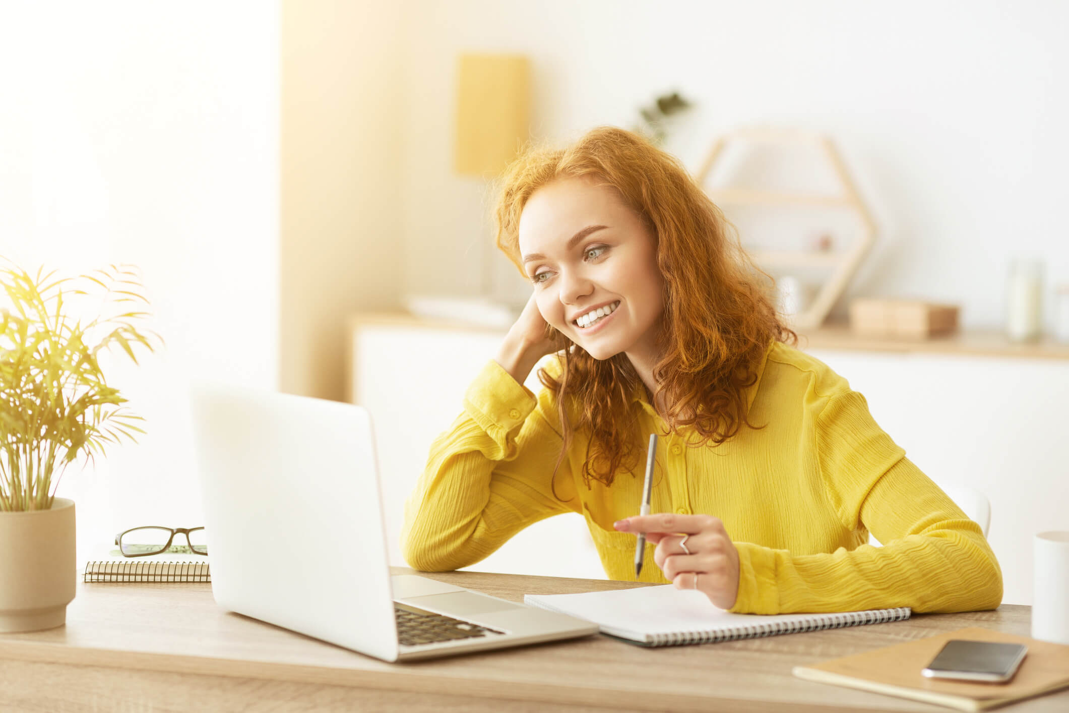 A smiling person sitting at a desk with a laptop