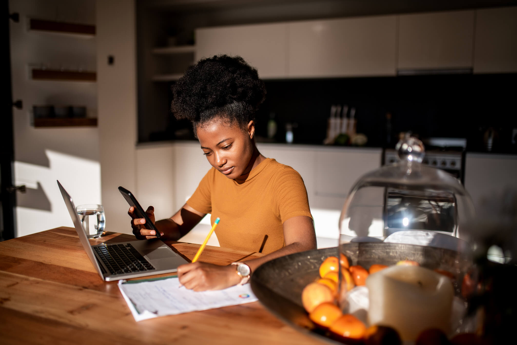 Young woman learning online with laptop and phone, she is taking notes in a notebook