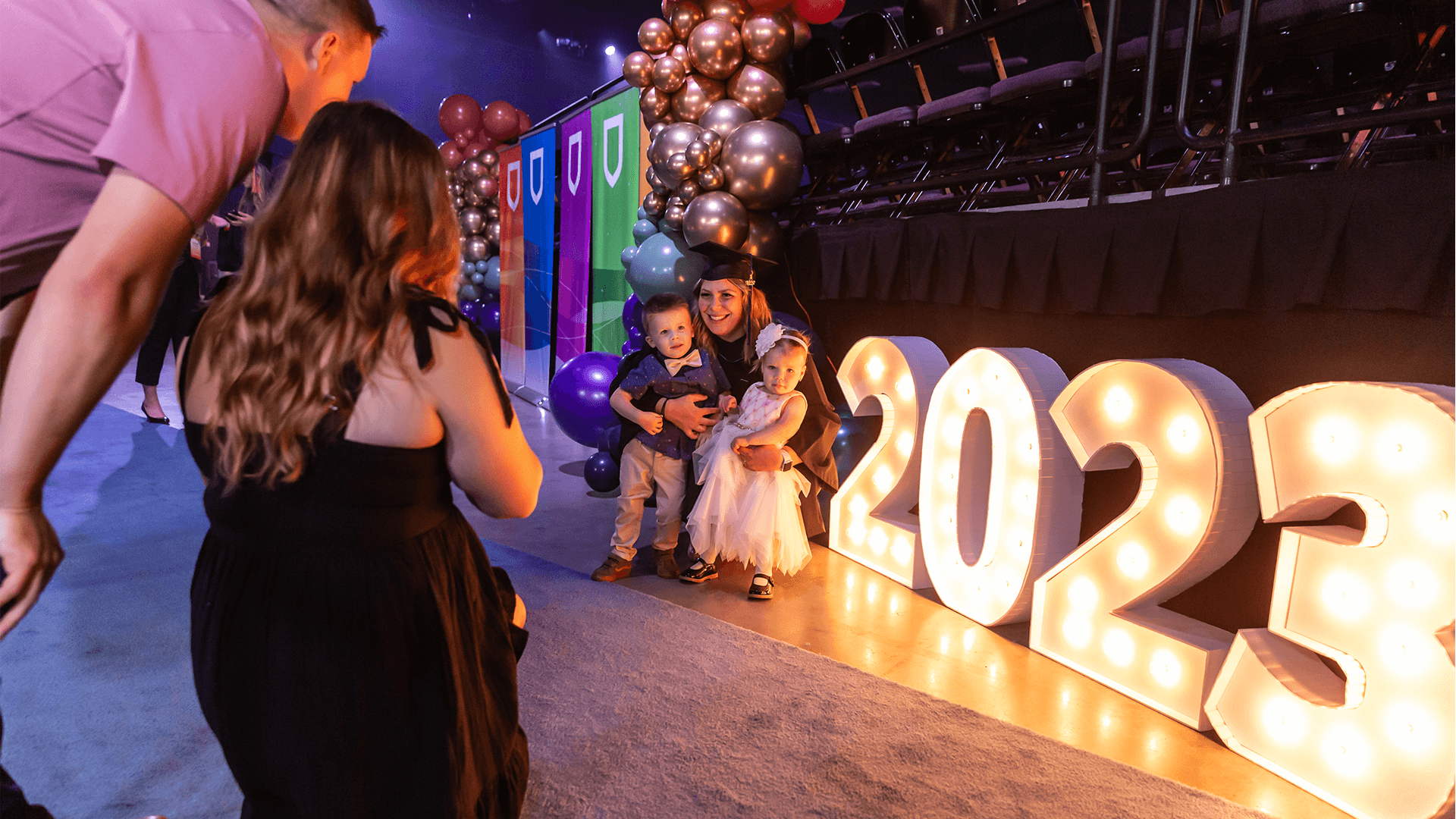 Shot of graduate with two young children next to 2023 lit letters