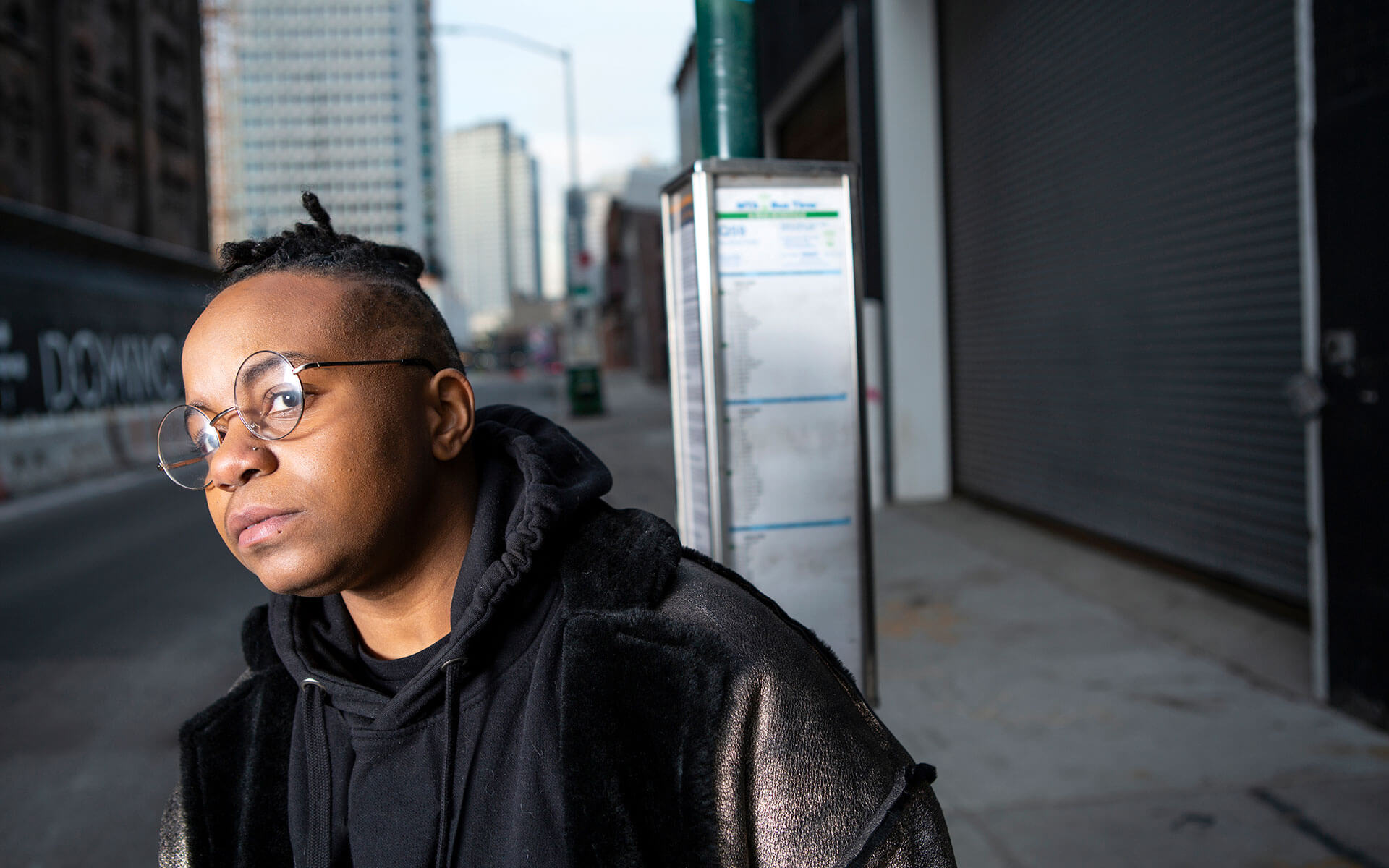 A transmasculine person waiting at a bus stop in an urban centre