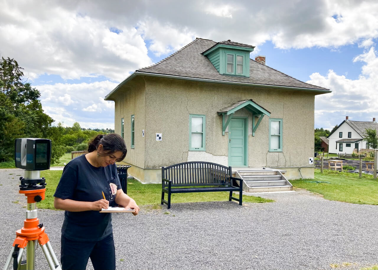 Image of a woman writing on a clipboard with a historical house in the background