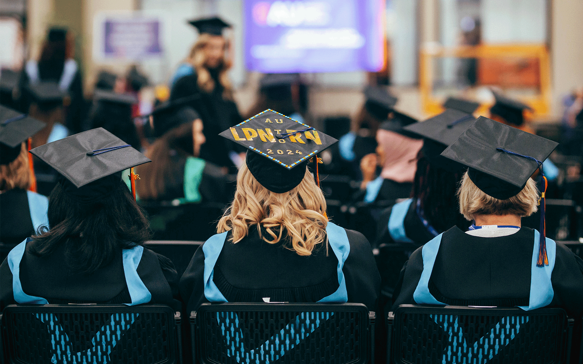 Back of seated grads. One of the graduation hats has the words LPN to RN 2024 on it