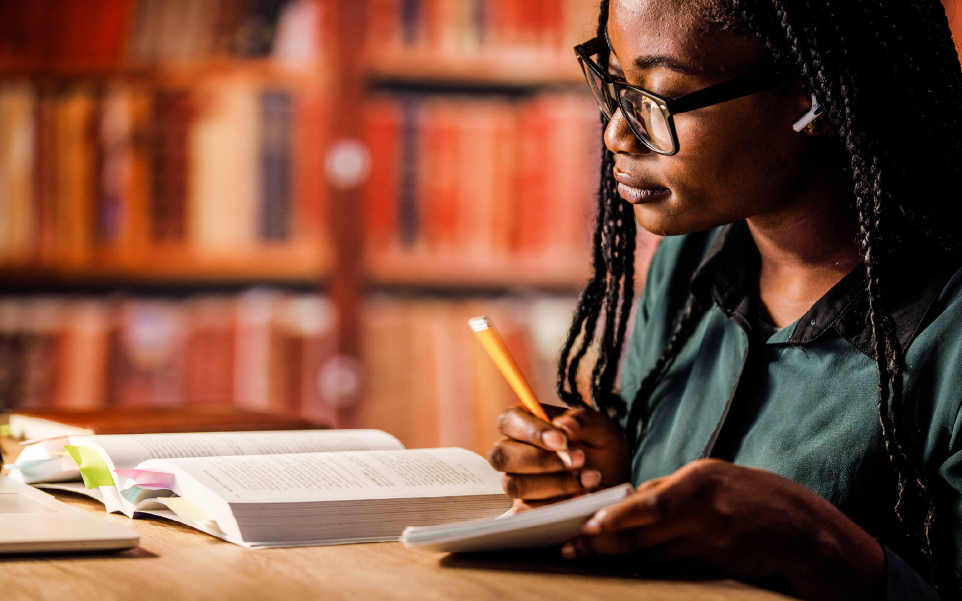 woman reading book in library while writing on a notebook working on citation