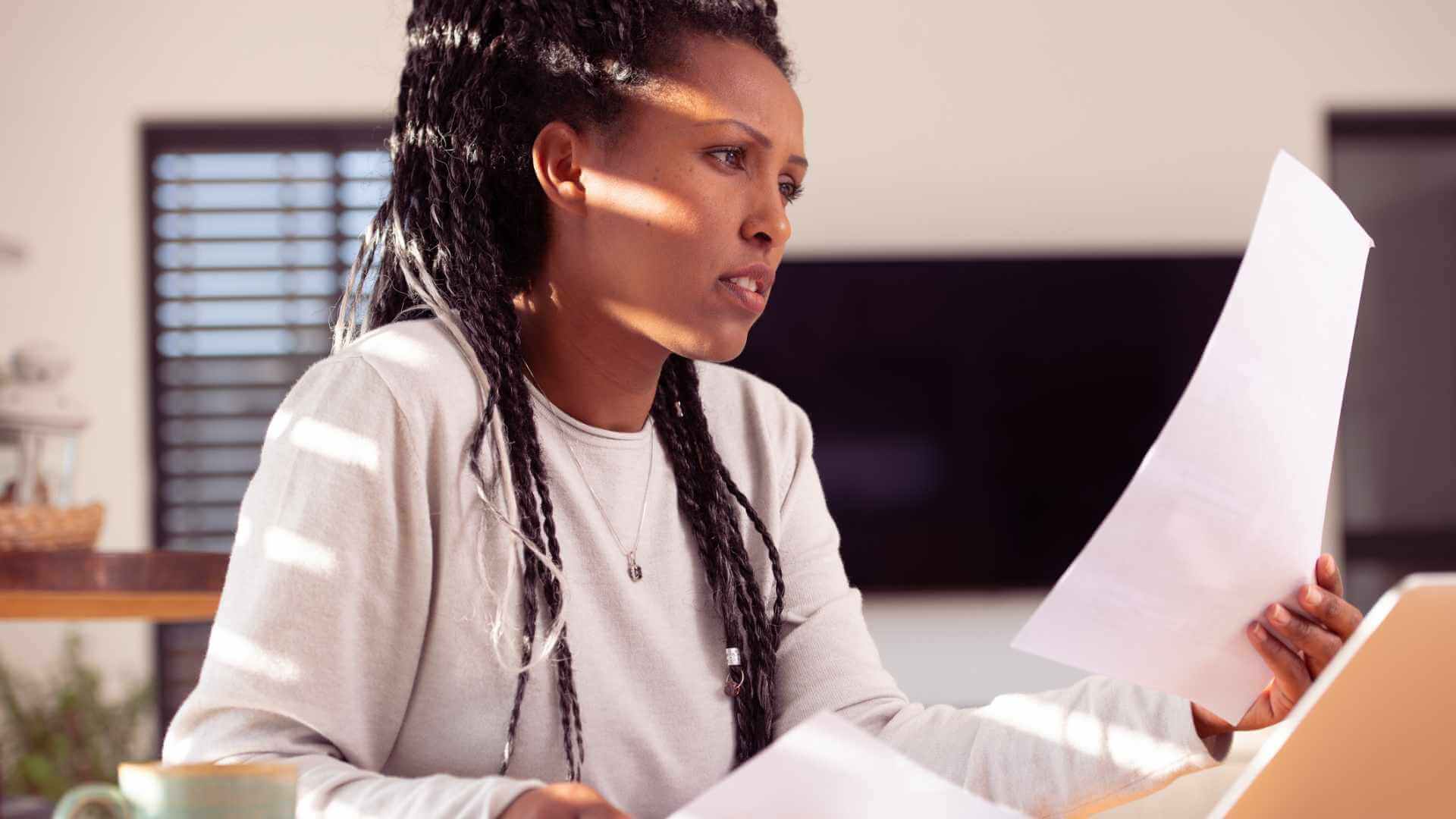 Person reading a document while working on a laptop in a well-lit office space.