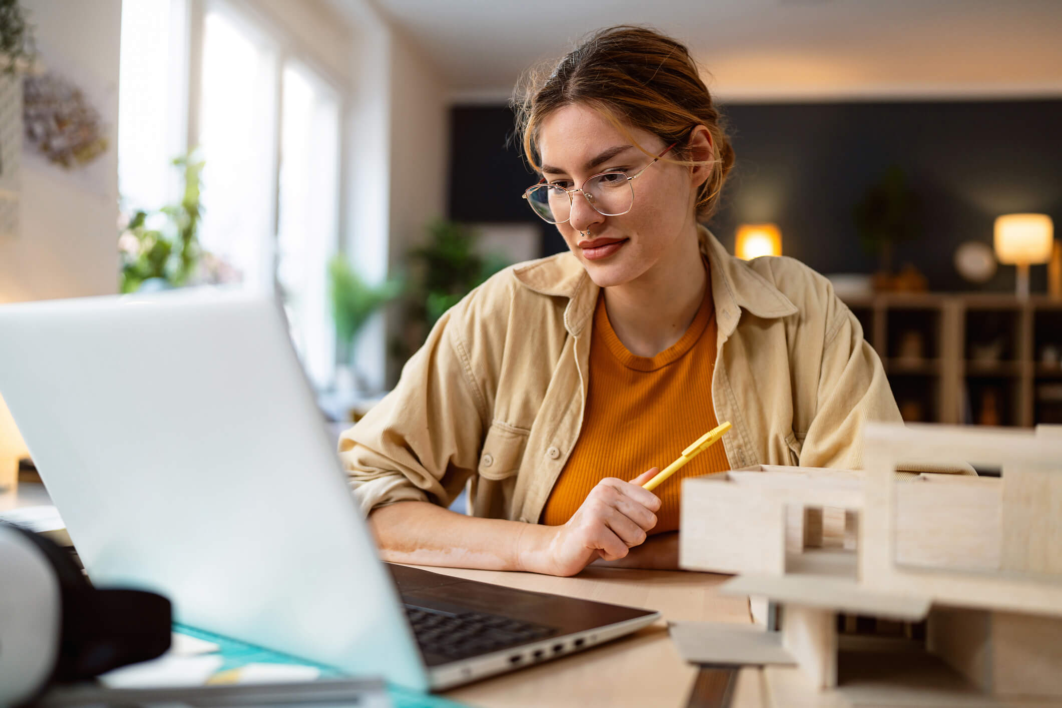 Woman with brown hair and glasses sitting at a table looking at her laptop