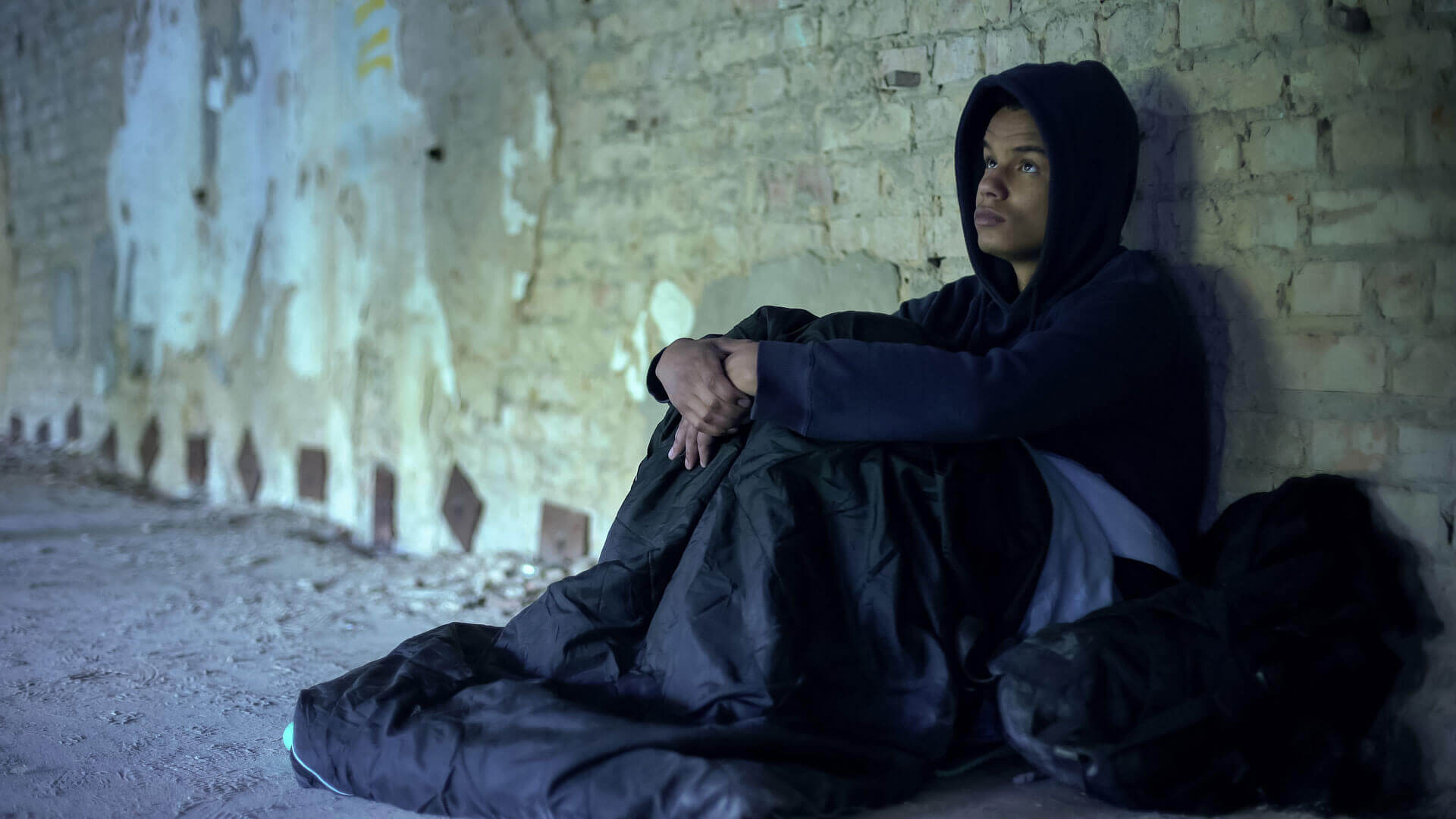 young person sitting up on the street with sleeping back